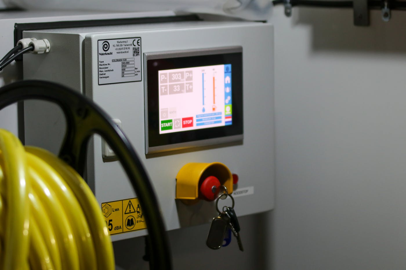 Industrial control panel with a digital screen, safety labels, and emergency-stop control.